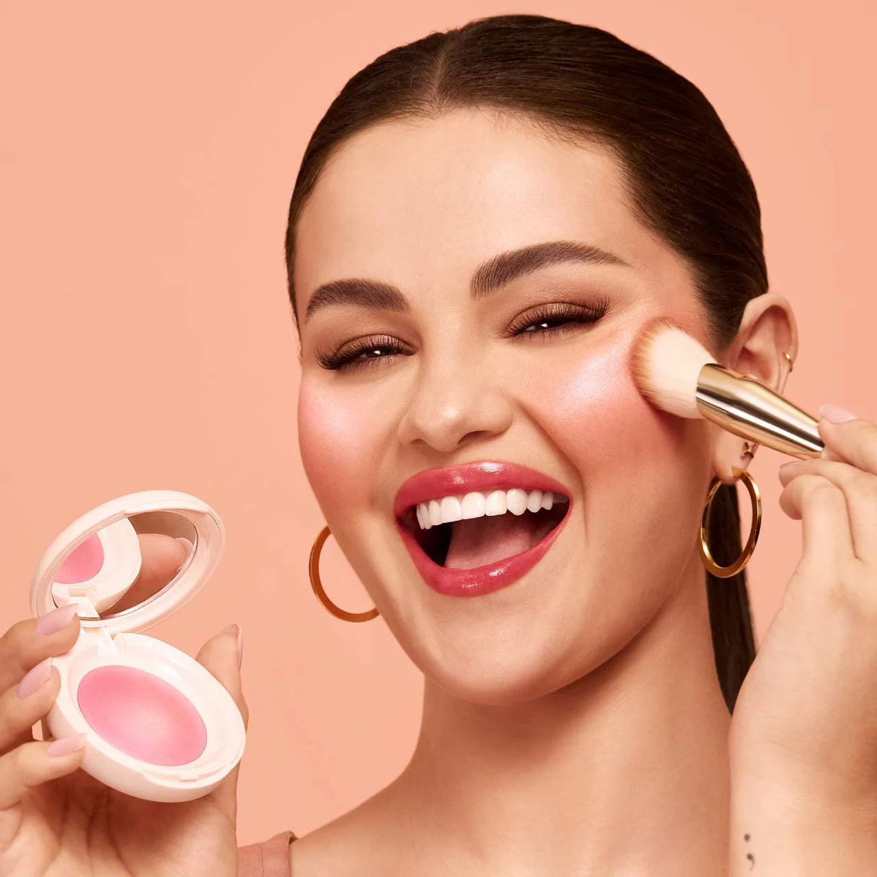 Model applying Rare Beauty Soft Pinch Luminous Powder Blush on cheeks