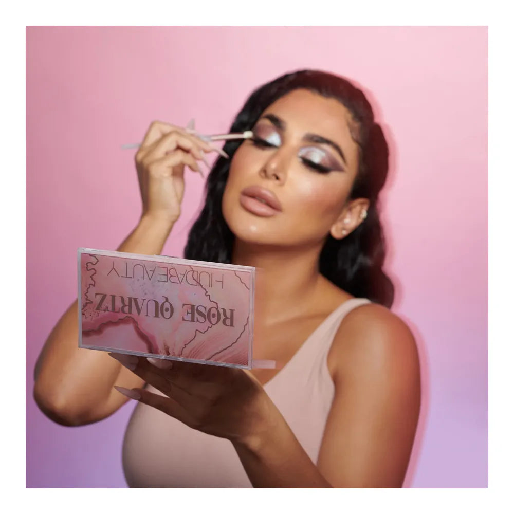 Model applying shimmer from HUDA BEAUTY Rose Quartz Eyeshadow Palette with an eyeshadow brush.