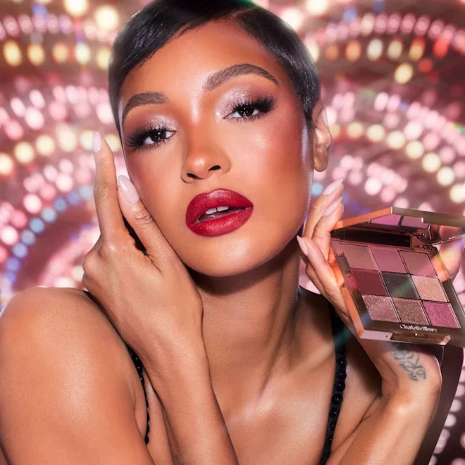 Model holding Charlotte Tilbury Pillow Talk Beautyverse Love Palette with a shimmering party eye look.