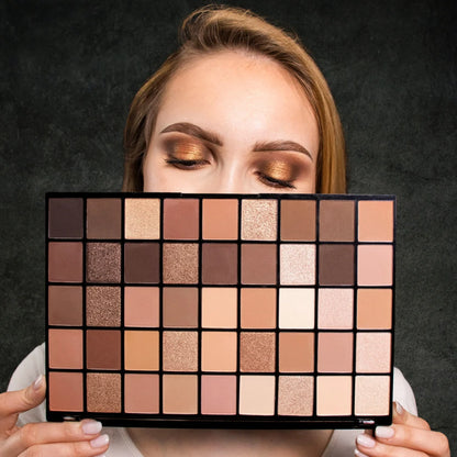 Model holding Makeup Revolution Maxi Reloaded Nudes Eyeshadow Palette with a bronze eye makeup look